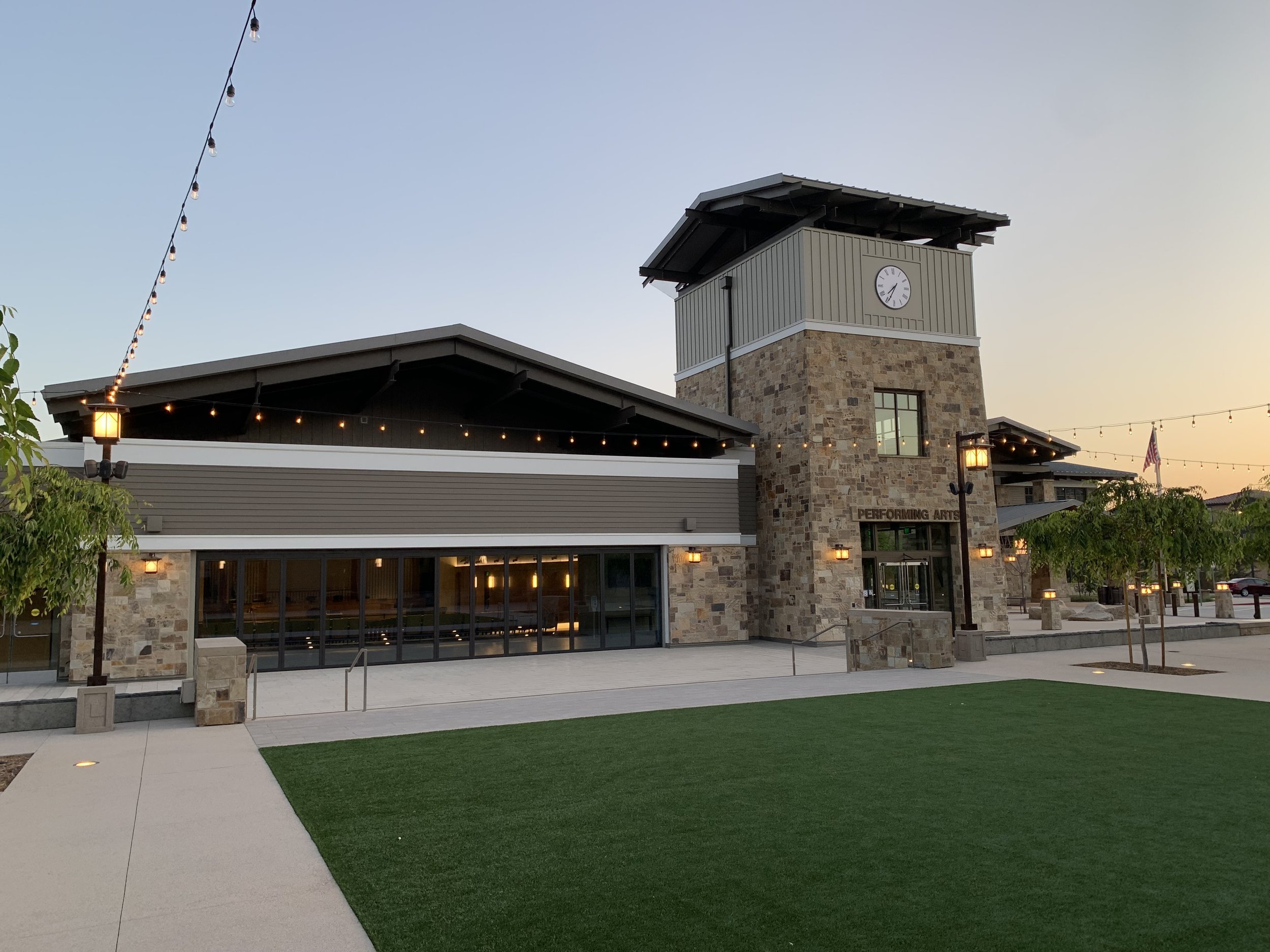 Modern performing arts center with clock tower, stone facade, and outdoor lighting at dusk.