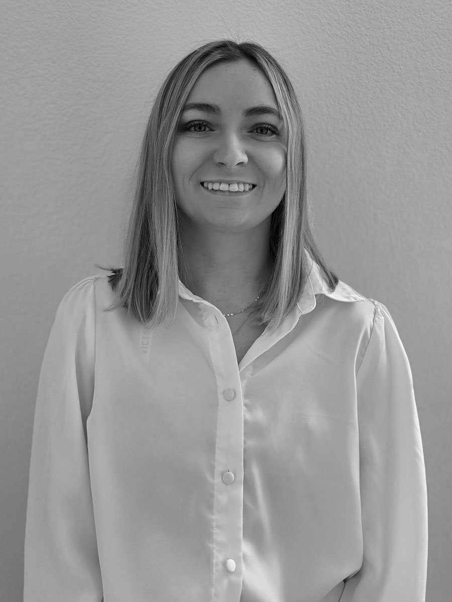 Black and white portrait of a person with long hair, wearing a white button-up shirt, smiling at the camera.